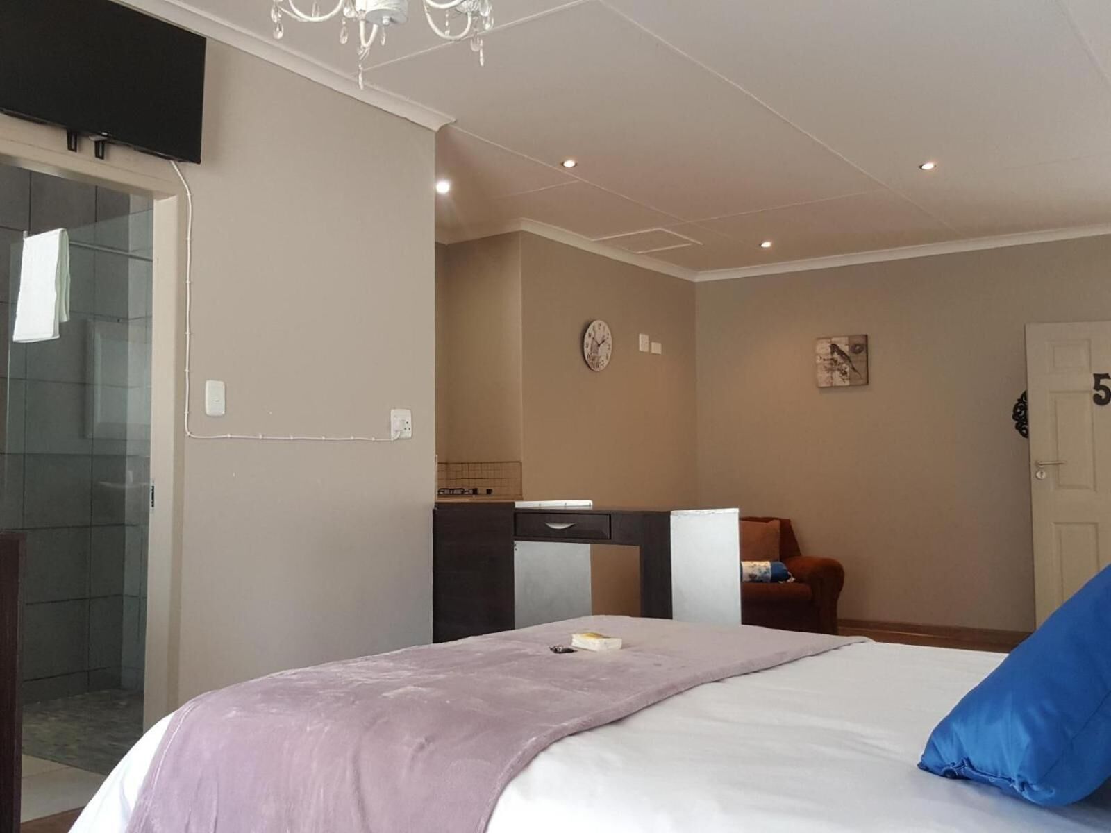 Un dormitorio con cama, escritorio, silla, reloj y puerta.