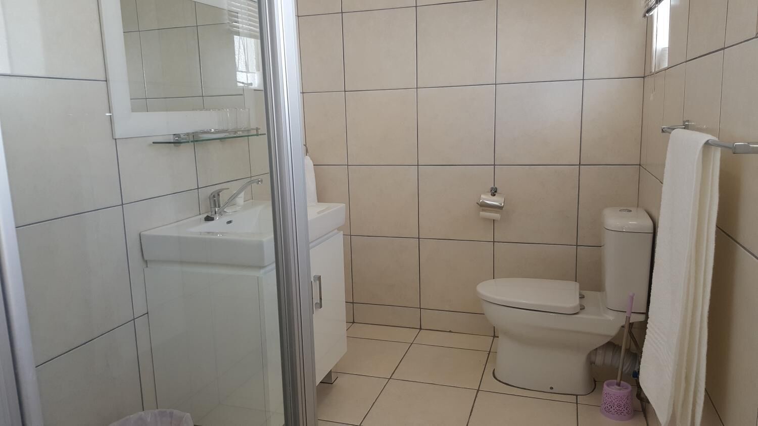 A bathroom with a toilet, sink, and glass shower enclosure.