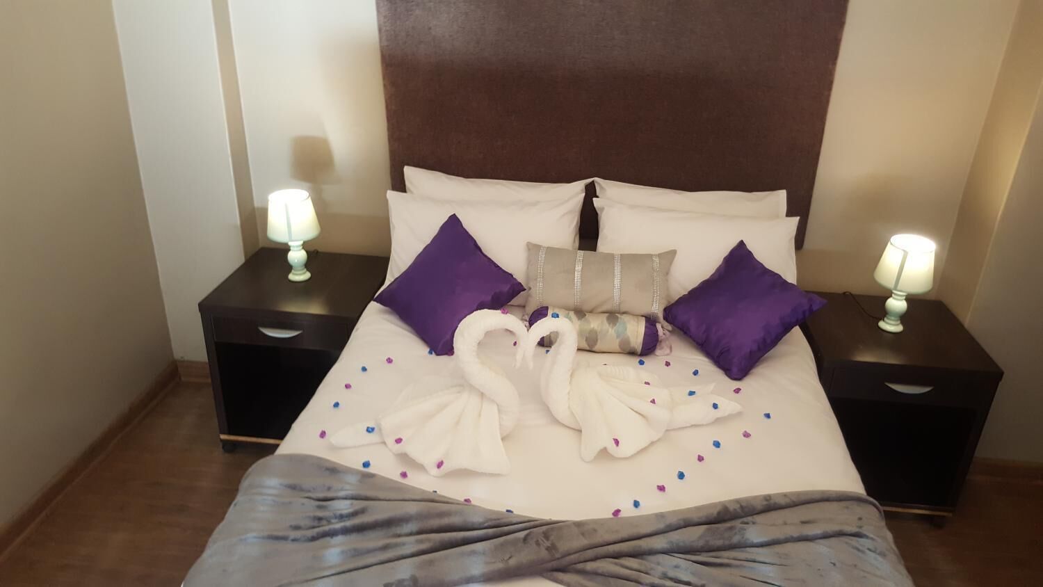 A neatly made bed with a brown headboard, two nightstands with lamps, and decorative pillows.