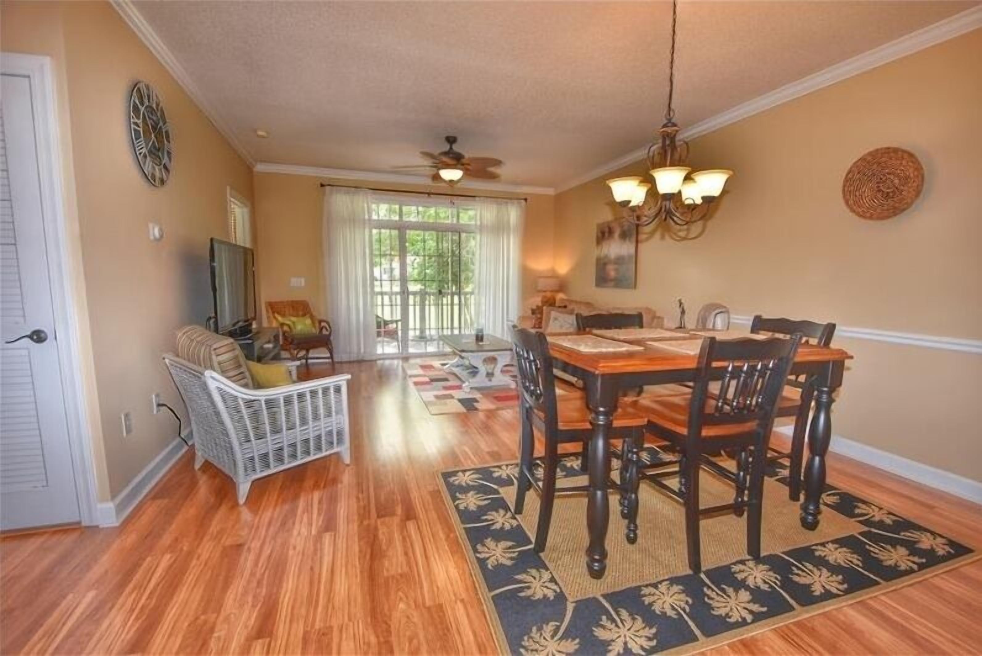 A dining area with a wooden table and chairs, a ceiling fan, and a chandelier.
