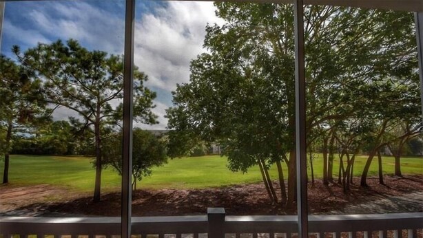 Une vue depuis un balcon doté d’une balustrade, donnant sur un espace verdoyant avec des arbres et un ciel dégagé.