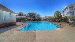 Une piscine rectangulaire à l’eau d’un bleu limpide, entourée de chaises longues et d’une terrasse dallée.