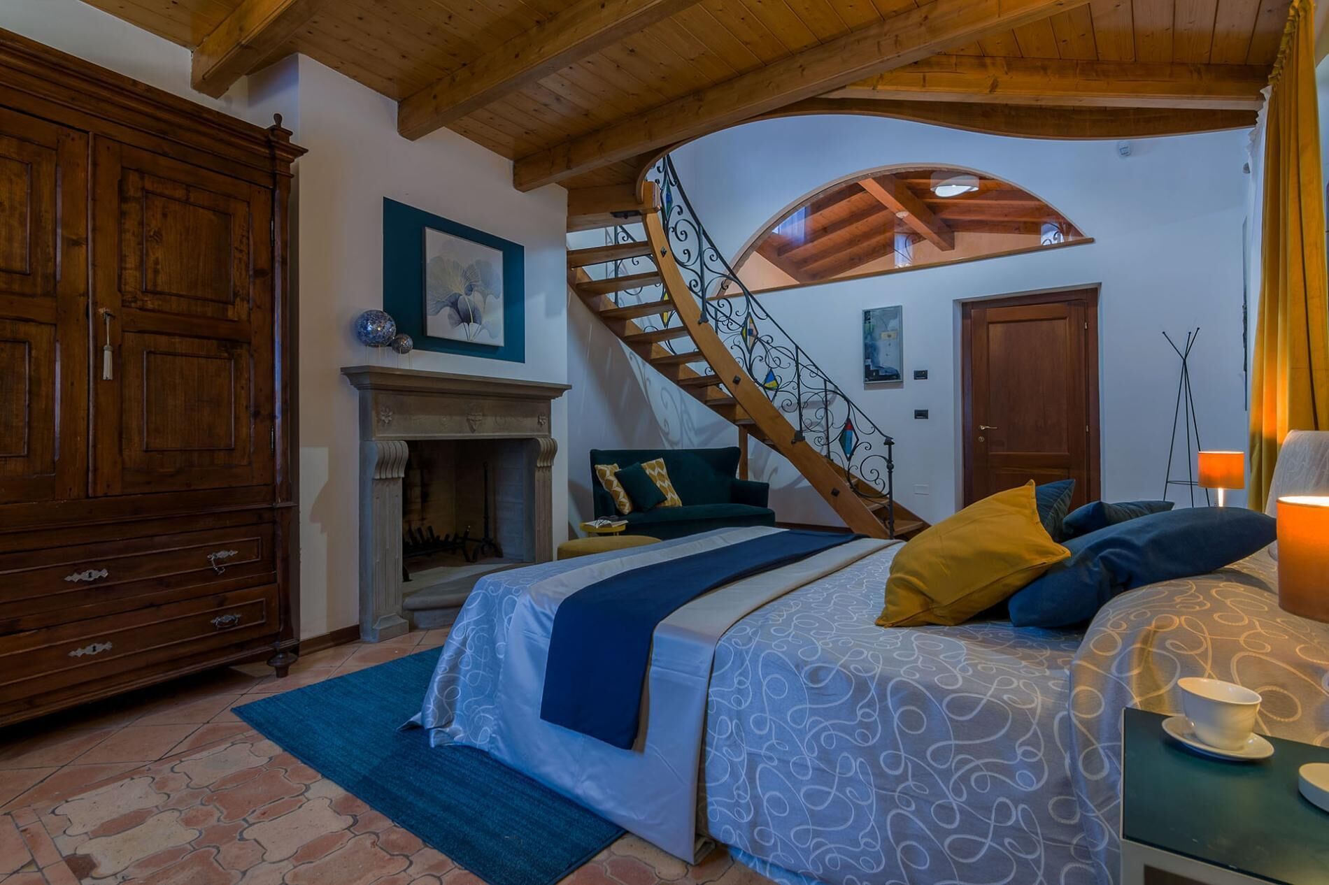 A bedroom with a bed, a fireplace, a wooden staircase, and a large wooden wardrobe.