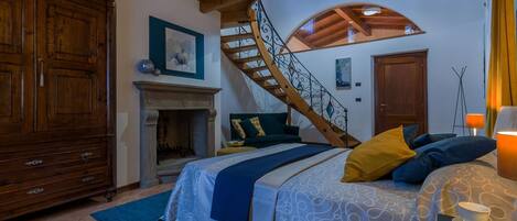 A bedroom with a bed, a fireplace, a wooden staircase, and a large wooden wardrobe.