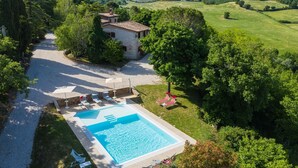 An aerial view of a villa with a swimming pool, surrounded by lush greenery and hills.