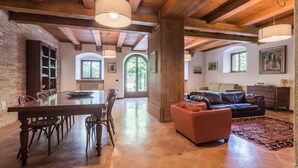 A spacious living area with a wooden ceiling, a dining table with chairs, a leather sofa, and a patterned rug.