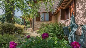 A rustic house with a brick facade, wooden shutters, and a garden with vibrant flowers.