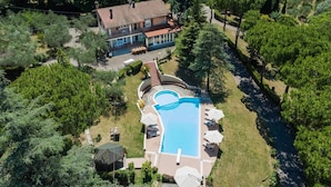 Vista aérea de una casa con piscina, rodeada de árboles y un jardín.