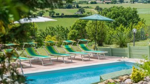 A pool area with lounge chairs and umbrellas, surrounded by greenery and a view of the countryside.
