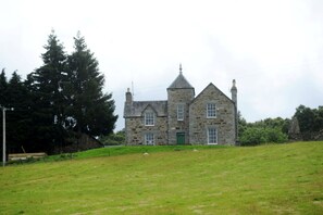 A stone building with a green door, surrounded by a grassy field and trees.