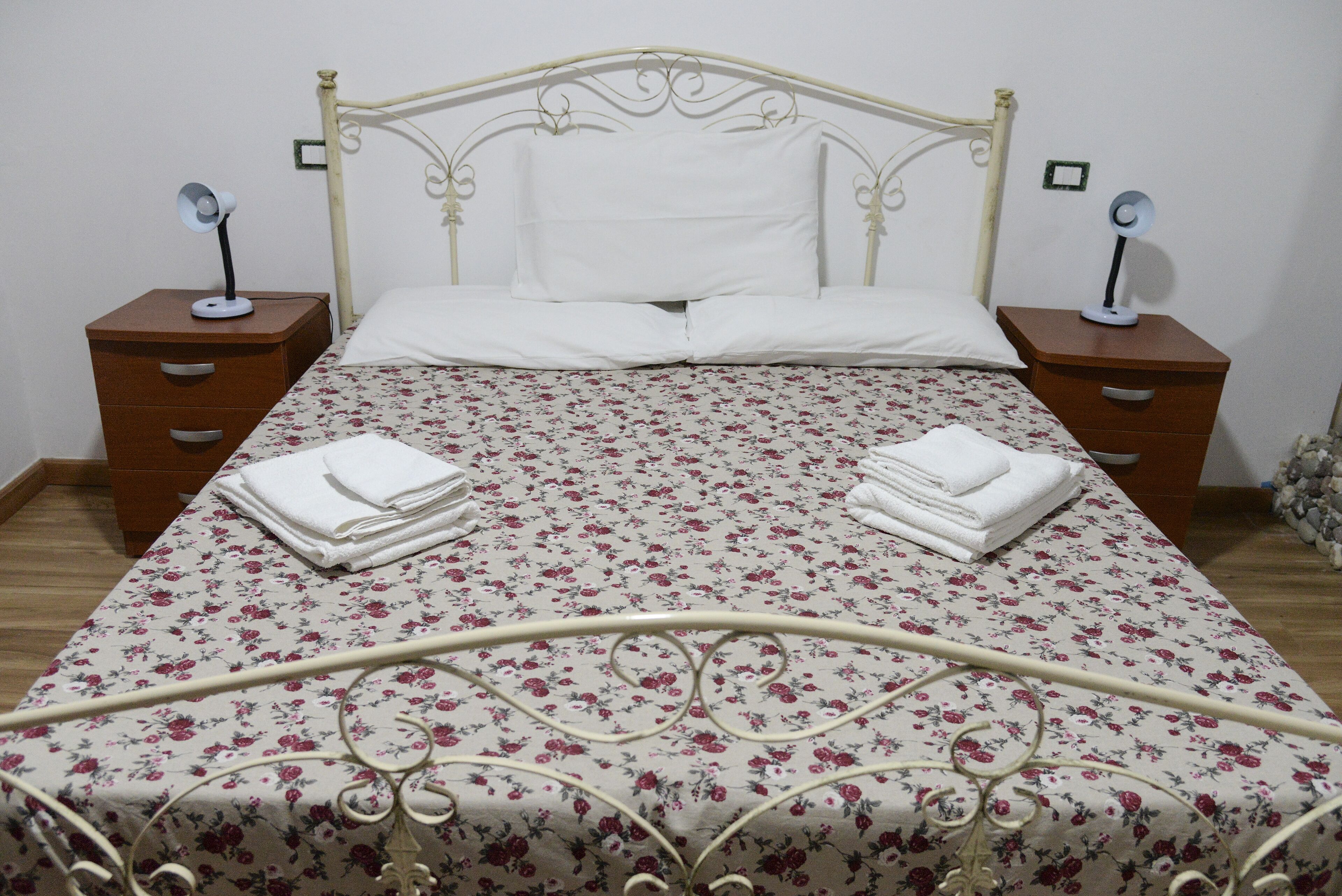 A neatly made bed with a floral bedspread, two bedside tables with lamps, and a wooden nightstand with drawers.