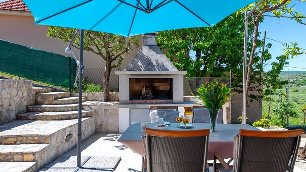 Un patio con chimenea de piedra, mesa y sillas al aire libre bajo una sombrilla azul.