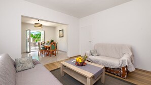 Una sala de estar con un sofá, una mesa de centro con fruta y un comedor al fondo.