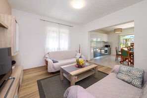 A modern living room with a sofa, coffee table, and TV. There is a kitchen in the background. - House MM (Ružic)