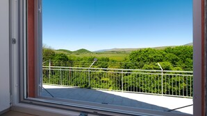 Un balcón con barandilla de metal que da a un paisaje verde con colinas.