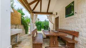 An outdoor patio with a stone floor, wooden benches, a table, and a view of greenery. - Villa Holiday Home Zvečanje (Zvecanje)