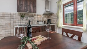 A kitchen with a wooden table, two wine glasses, a bottle of wine, and a cutting board with cheese. - Villa Holiday Home Zvečanje (Zvecanje)