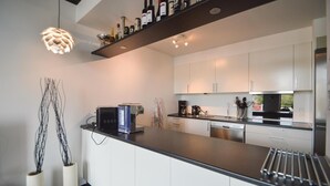 A modern kitchen with white cabinets, a black countertop, and a coffee machine. There are two decorative vases on the counter. - Stunning apartment in Rømø with house sea view (Rømø)