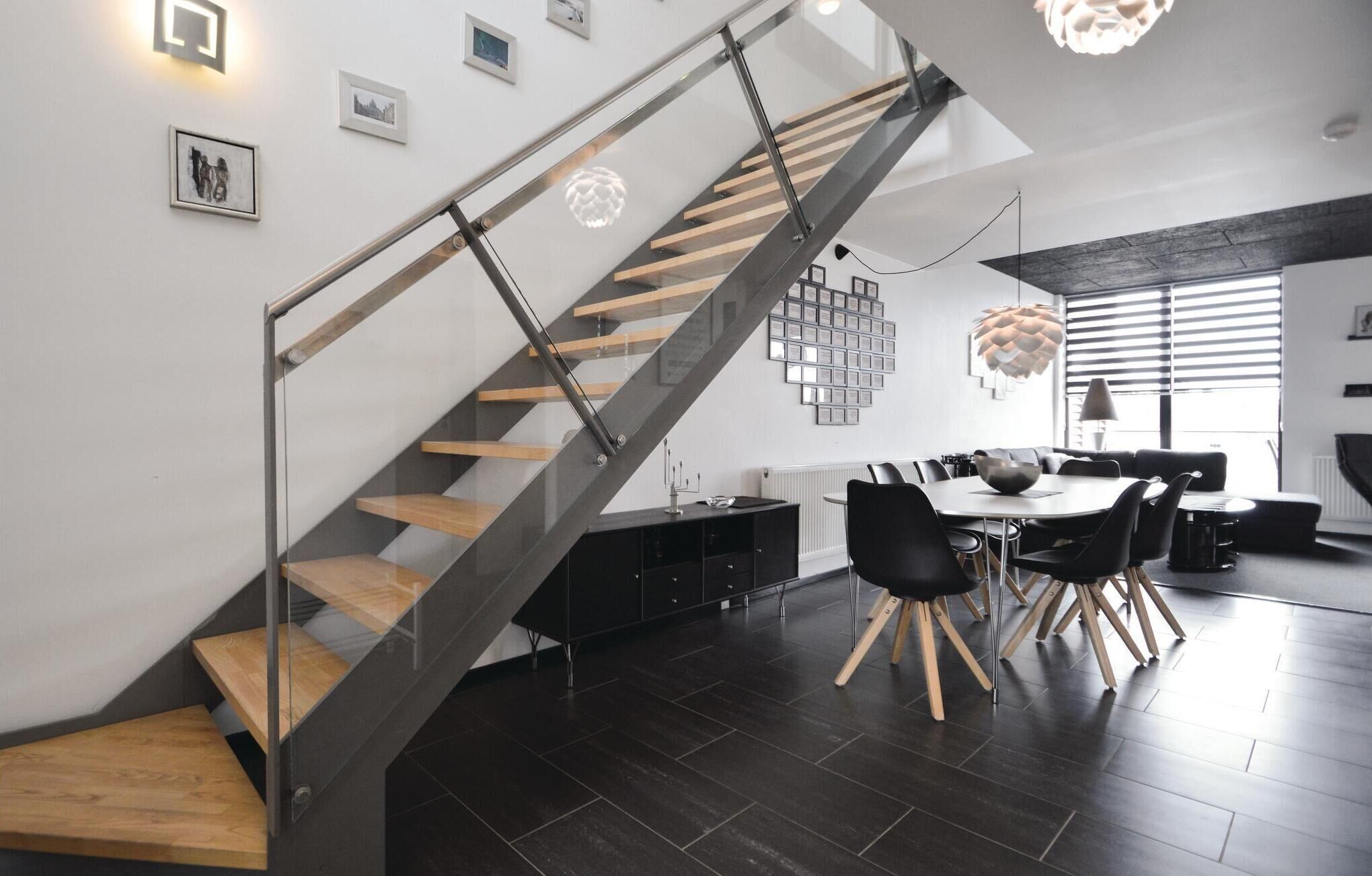 Een modern interieur met een glazen en houten trap, een eetgedeelte met een ronde tafel en zwarte stoelen, en een keuken met een zwart aanrecht en kastjes.