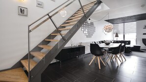 A modern interior with a glass and wood staircase, a dining area with a round table and black chairs, and a kitchen with a black countertop and cabinets. - Stunning apartment in Rømø with house sea view (Rømø)