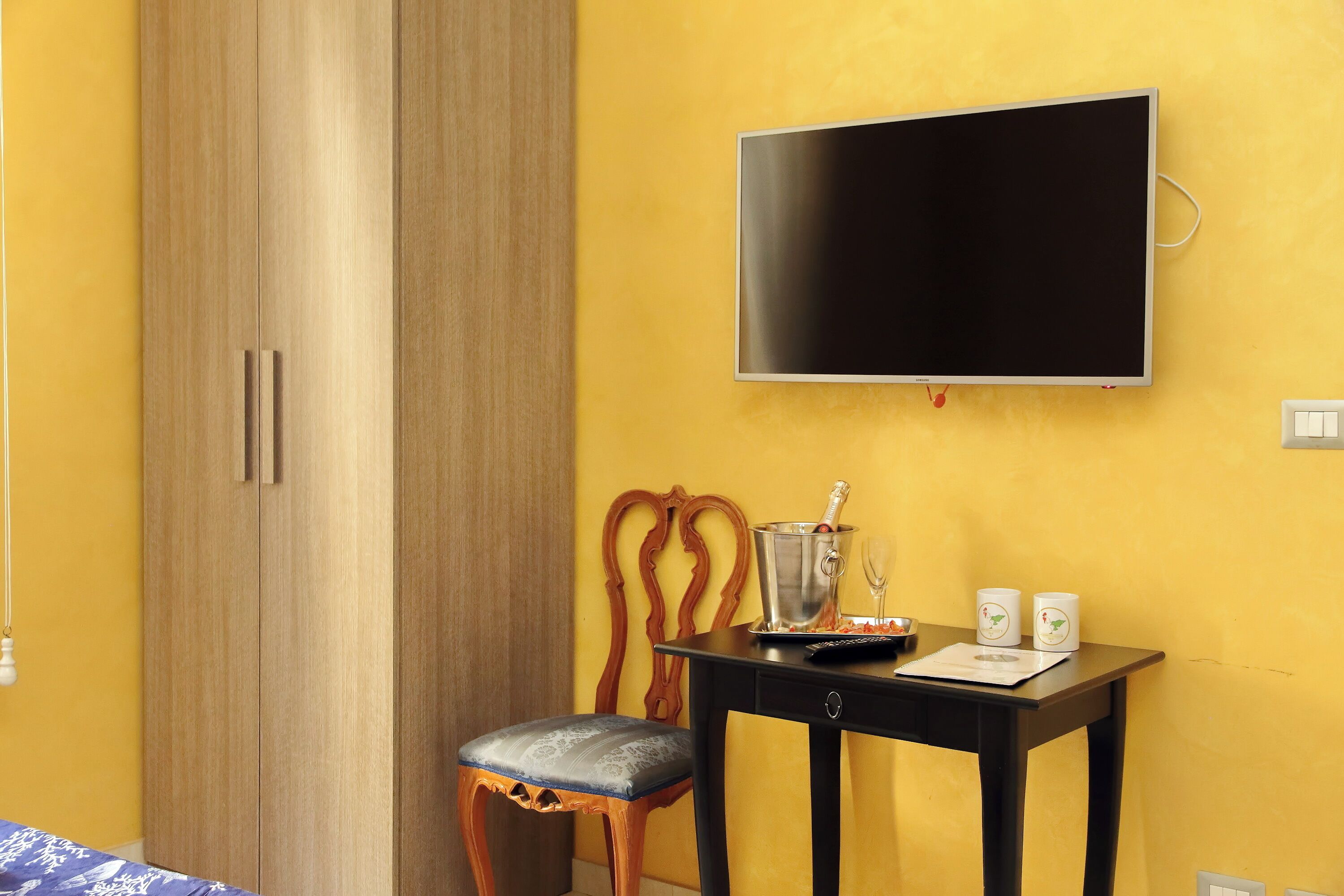 Una habitación con un armario de madera, un televisor montado en la pared, una mesita con un mando a distancia, un vaso y dos tazas.