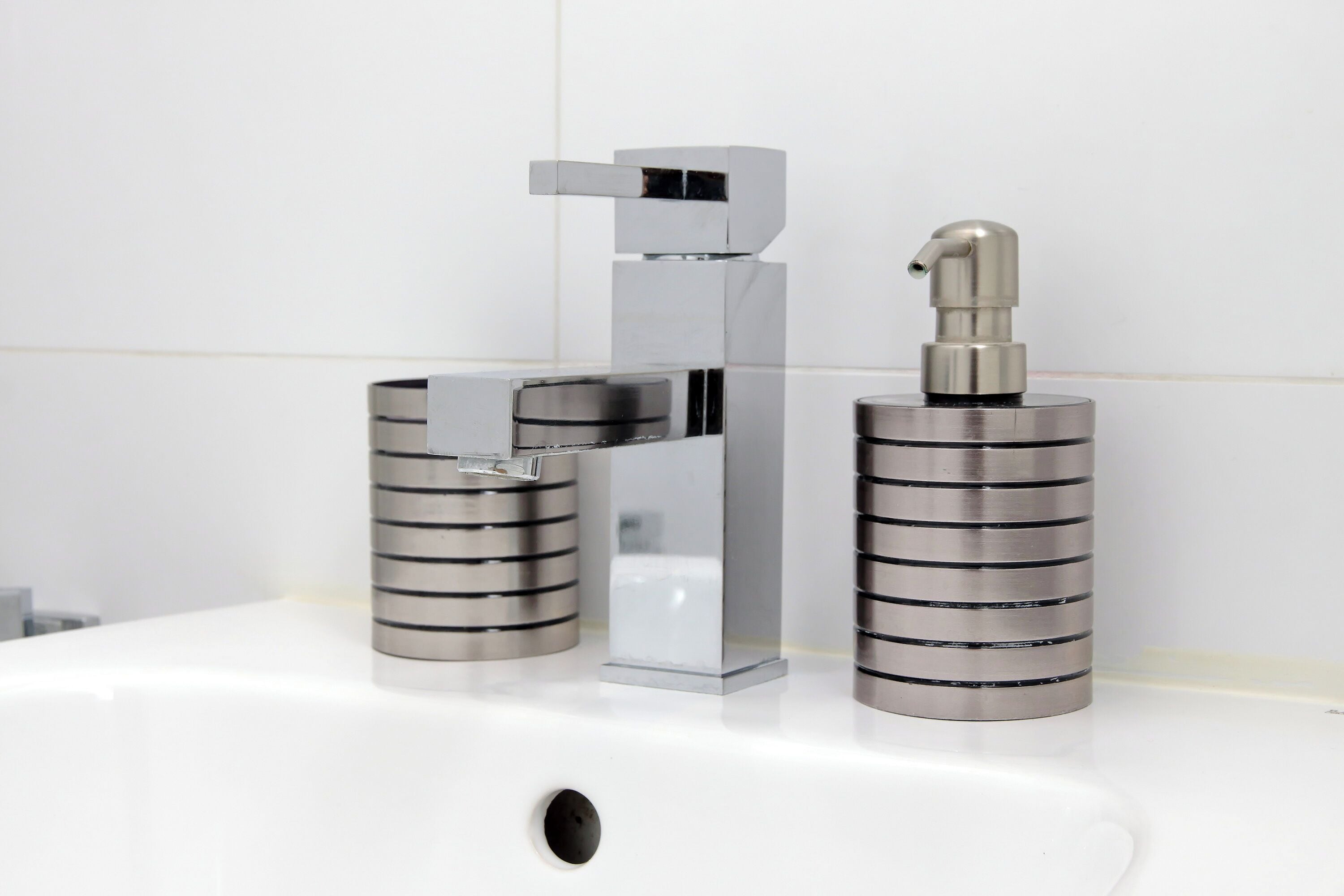 Un baño moderno con grifo de cromo, dispensador de jabón y soporte para papel higiénico sobre un lavabo blanco.