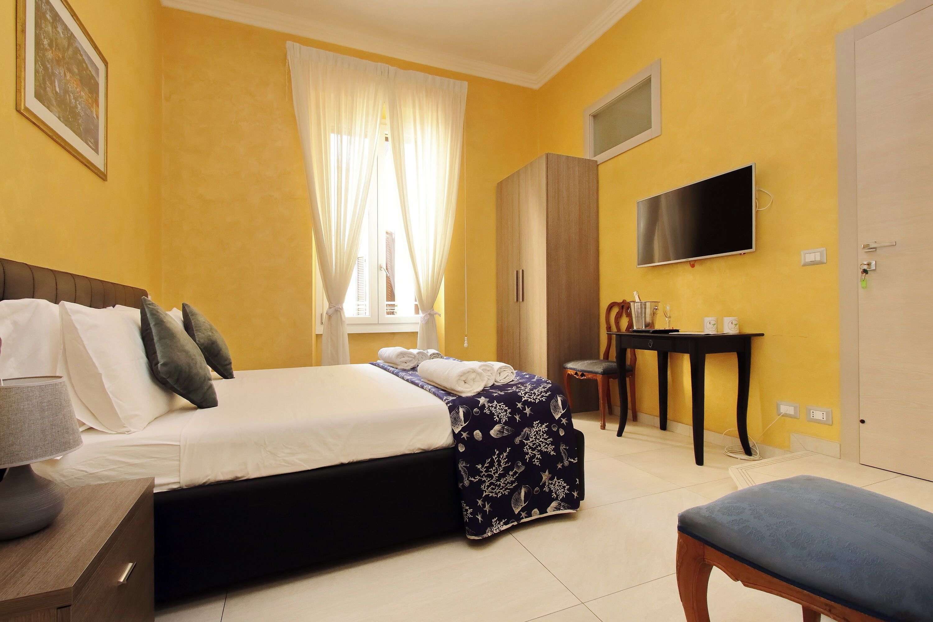 Une chambre d’hôtel comprenant un lit, une table de chevet, une chaise, un bureau, une télévision, une armoire et un banc.