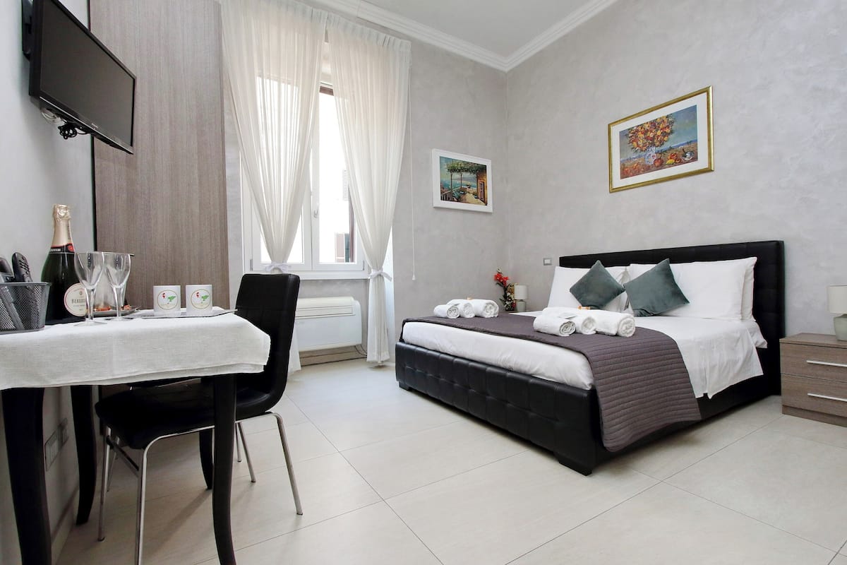 A hotel room with a bed, a desk with a chair, a TV mounted on the wall, and artwork on the walls.