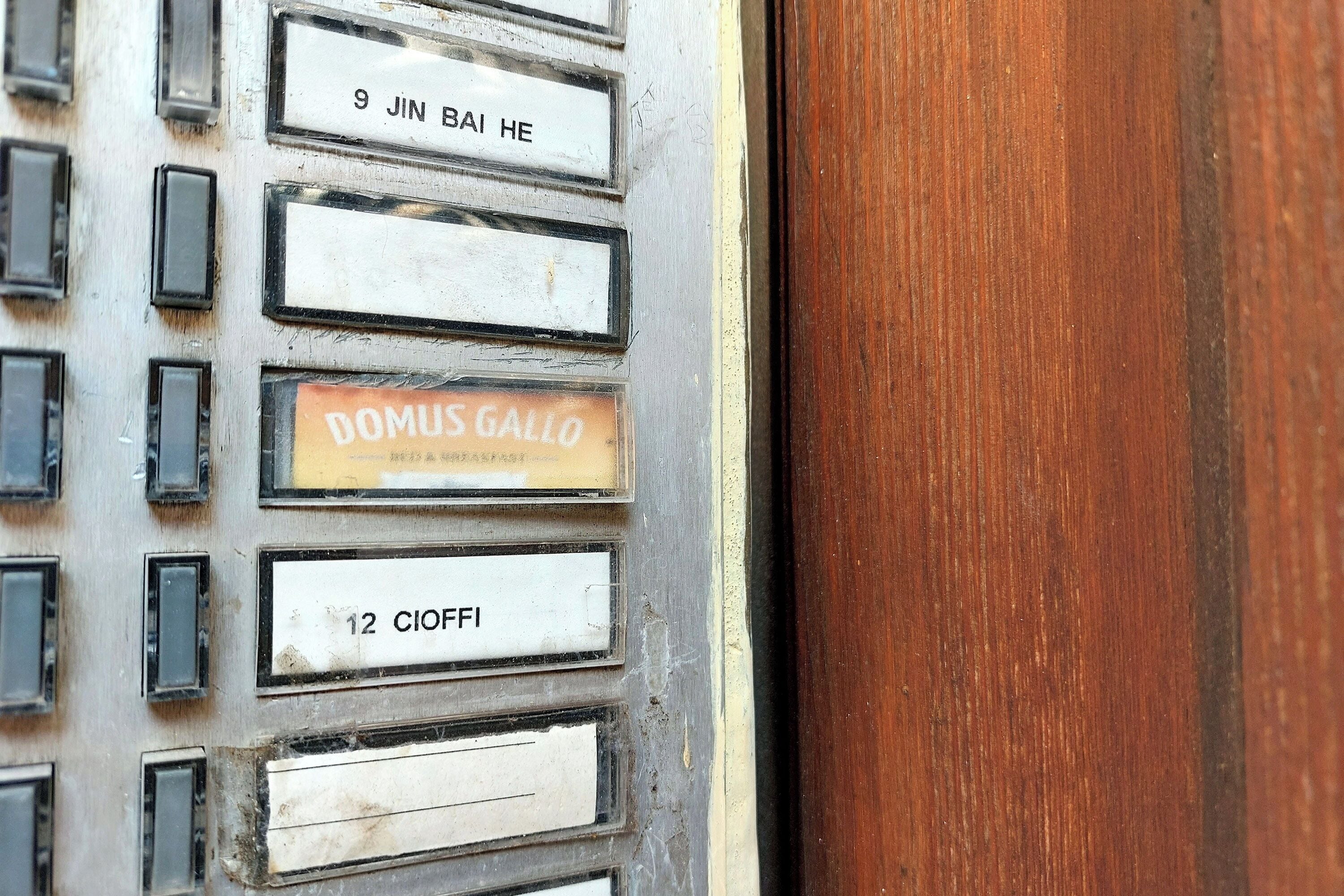 Une vue rapprochée d’une porte avec des plaques numérotées indiquant les numéros de chambre, notamment « 9 Jin Bai He », « Domus Gallo » et « 12 Cioffi ».