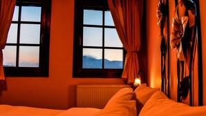 Una habitación con dos ventanas, una cama con ropa de cama blanca y una lámpara fijada a la pared.