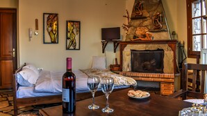Un dormitorio con chimenea de piedra, una cama con ropa de cama blanca, una botella de vino y dos copas de vino sobre una mesa de madera.