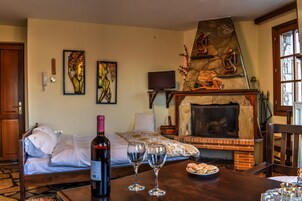 A bedroom with a stone fireplace, a bed with white linens, a bottle of wine, and two wine glasses on a wooden table.