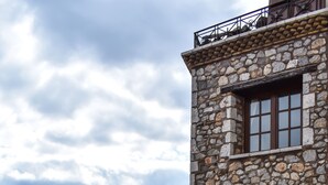 Un edificio de piedra con puerta y ventanas de madera, una escalera de piedra y una barandilla de metal que da a un paisaje montañoso.