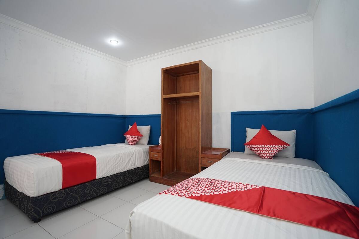 Une chambre d’hôtel avec deux lits simples, une armoire en bois et un mur d’accent bleu.