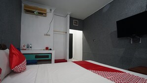 Une chambre d’hôtel avec un lit, un téléviseur fixé au mur, un bureau avec une chaise et une fenêtre.