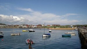 A harbor with several boats anchored in calm waters, a sandy beach, and buildings in the background. - Helena Cottage, Elie, Fife (Earlsferry)