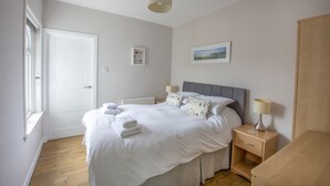 A bedroom with a bed, bedside tables, a window, and a door. - Helena Cottage, Elie, Fife (Earlsferry)