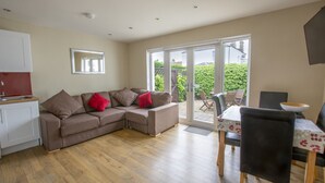 A modern living room with a sectional sofa, a dining table with chairs, and a sliding glass door leading to a garden. - Helena Cottage, Elie, Fife (Earlsferry)