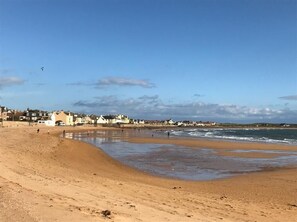 Uma praia de areia com alguns edifícios ao fundo.