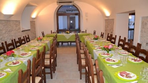 Uma sala de jantar com mesas longas, cadeiras e vista pela janela.