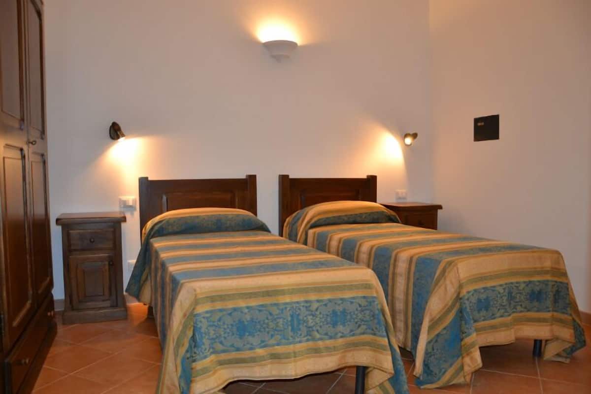 A room with two beds, each with a striped bedspread, a nightstand, and a wall-mounted light fixture.