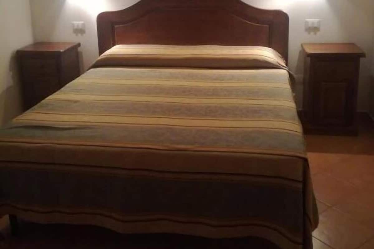 A single bed with a wooden headboard and two bedside tables, each with a wall-mounted light.