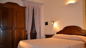 Quarto com guarda-roupa de madeira, cama com colcha floral e luminária fixada na parede.