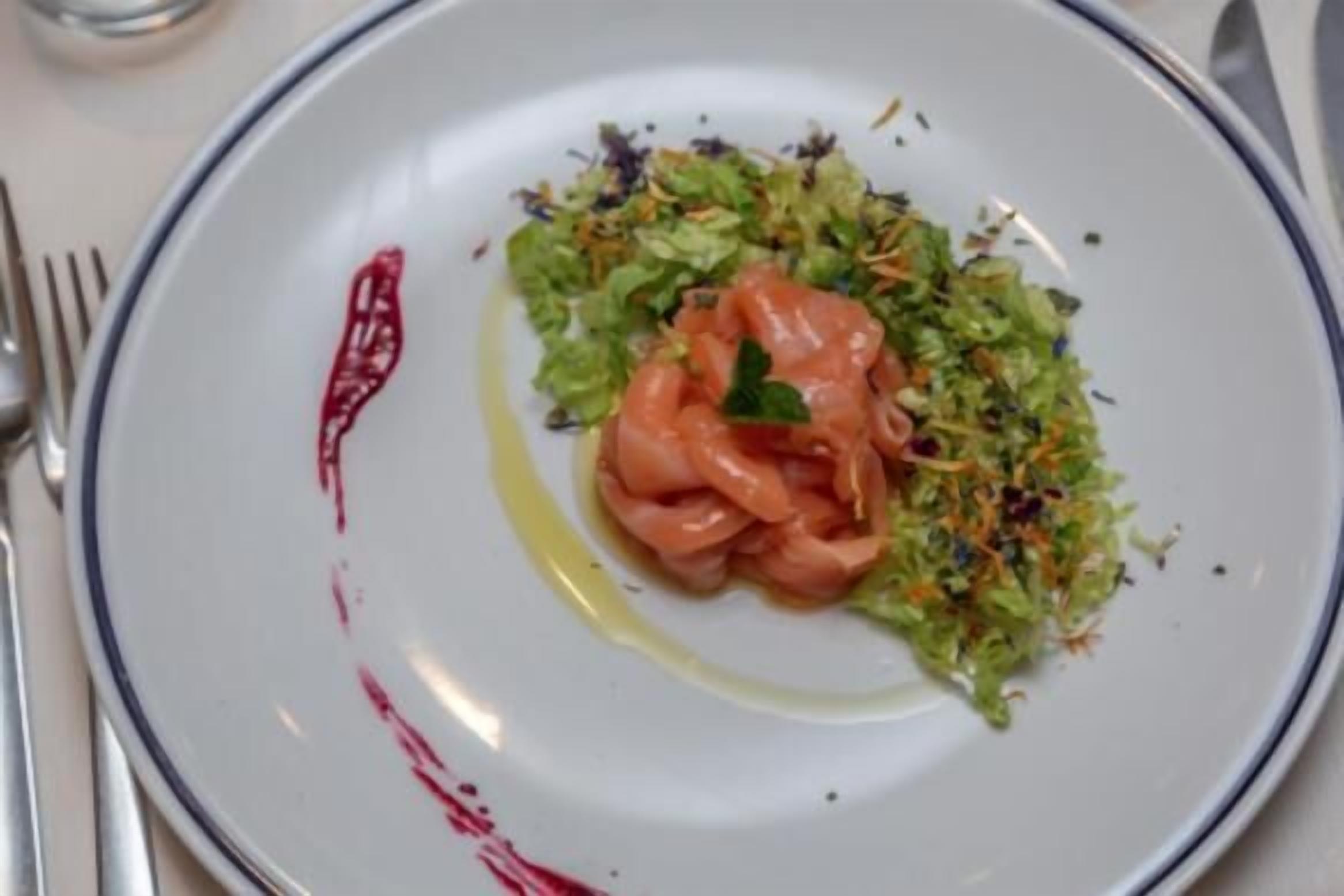A plate with a salad and salmon, accompanied by a fork and knife on the table.