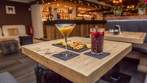 A bar area with a wooden table displaying a cocktail, a glass of red drink, and some pastries. - Hotel Gran Roc (Sestriere)