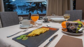 A dining table set with an omelette, a glass of orange juice, a cup of coffee, and a plate of food. - Hotel Gran Roc (Sestriere)
