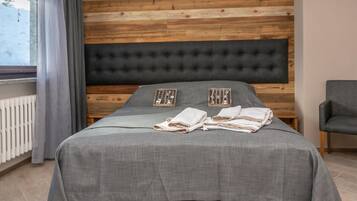 A bedroom with a wooden wall, a tufted headboard, a grey bedspread, and a grey chair.