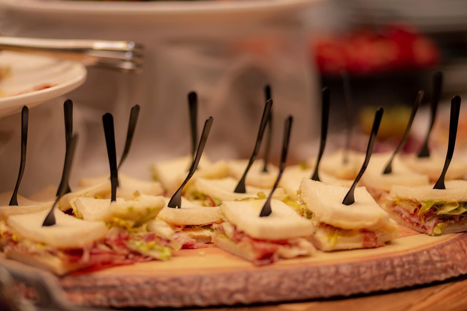 A tray of sandwiches with toothpicks, arranged on a wooden board.