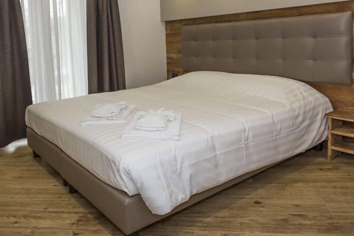 A neatly made bed with white linens and folded towels, a wooden headboard, and a wooden floor.