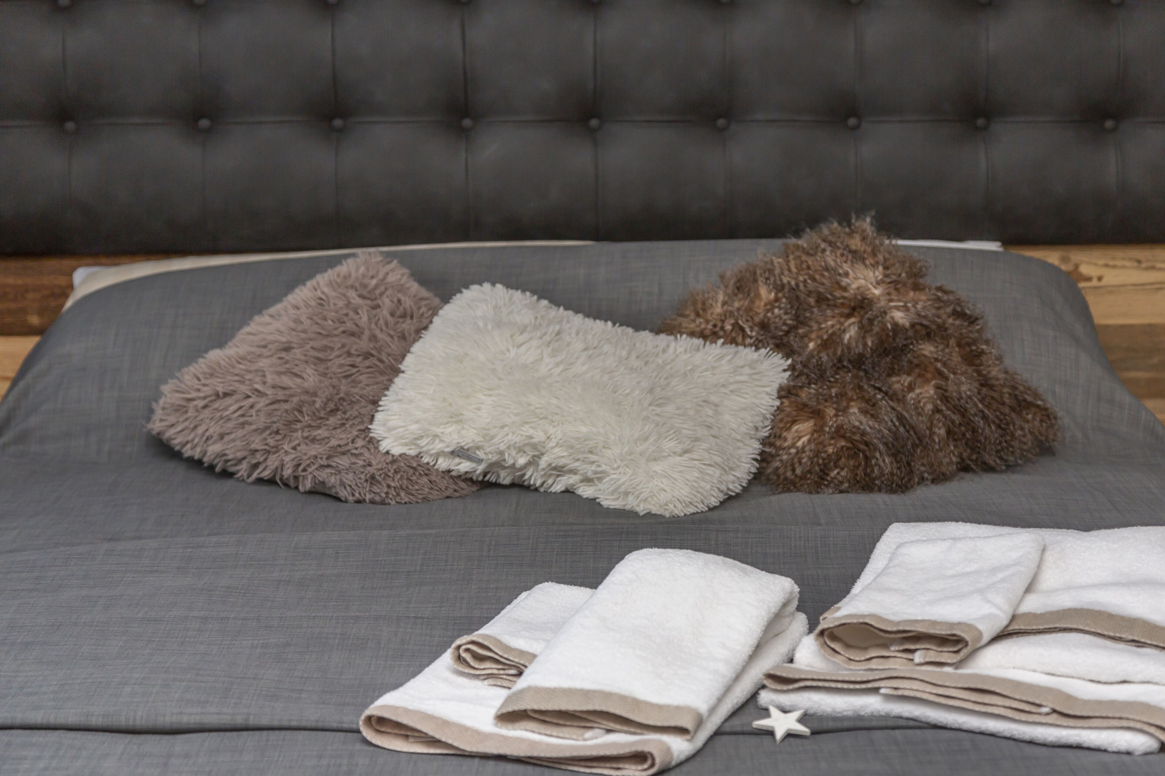 Una cama con sábanas grises y tres almohadas mullidas en diferentes tonos.